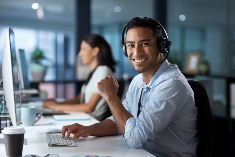 A smiling man with headset sitting at a desk, interacting with a computer taking reservations for a taxi company.