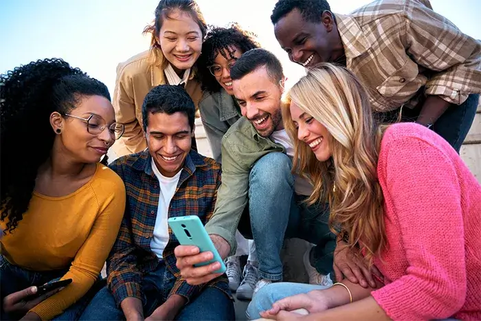 A group of young individuals gathered together, using one cell phone to book a taxi ride in Florida